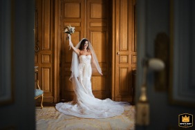 Bride holding her bouquet, posing indoors by large wooden doors at Chateau La Durantie, France.